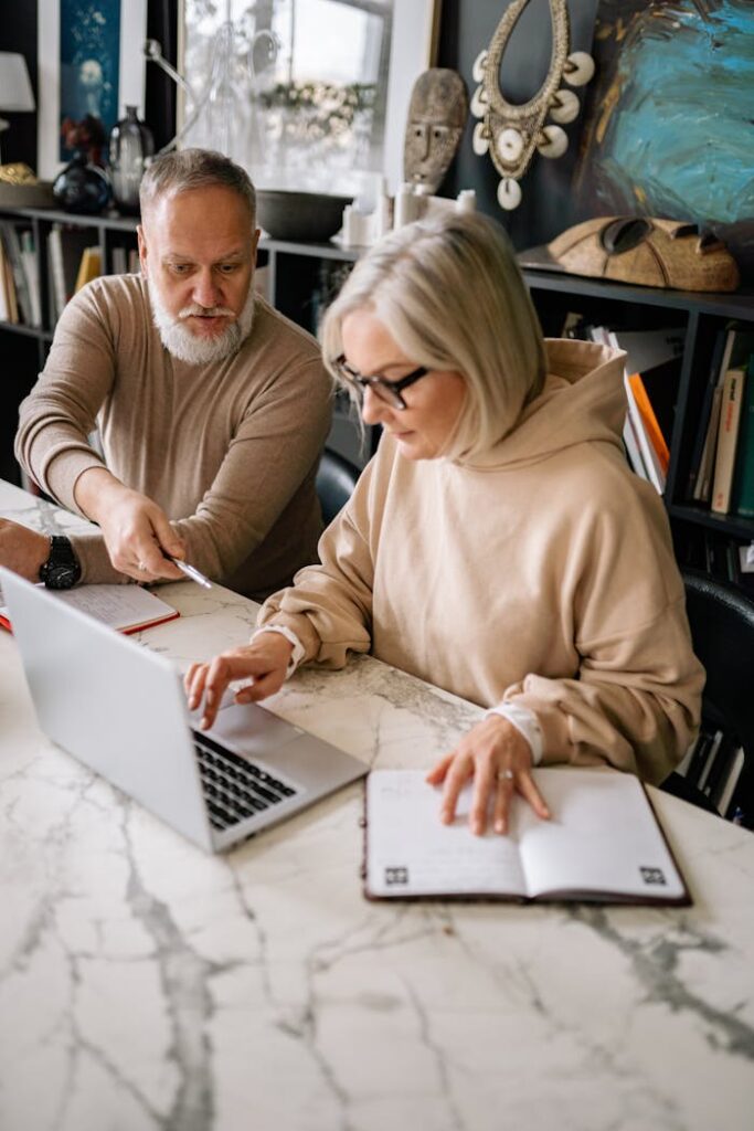 Elderly couple engages in online planning at home, using a laptop. Comfortable indoor setting.